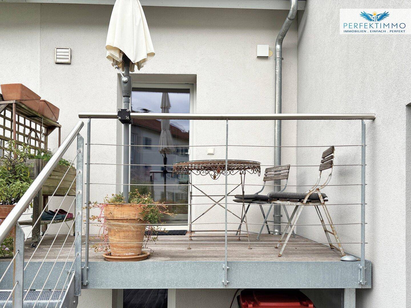 Kleiner Balkon mit Metallgeländer, Tisch und Stühlen, ideal für eine Kaffeepause.