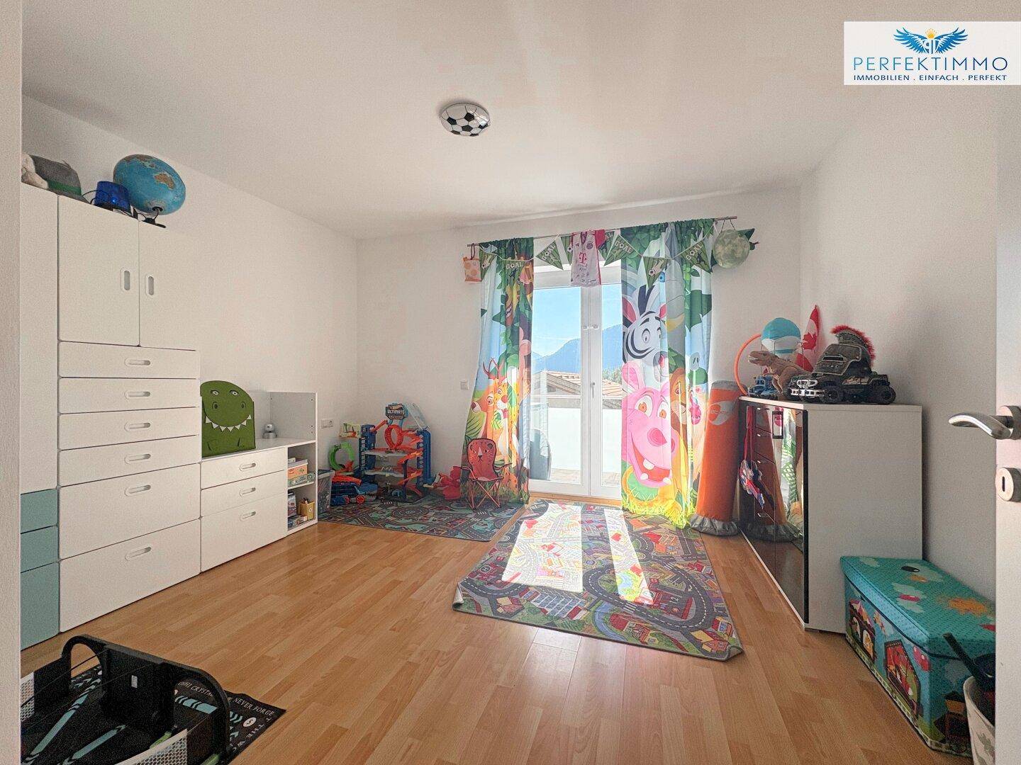Kinderzimmer mit Holzboden, bunten Vorhängen und Zugang zu einem Balkon.