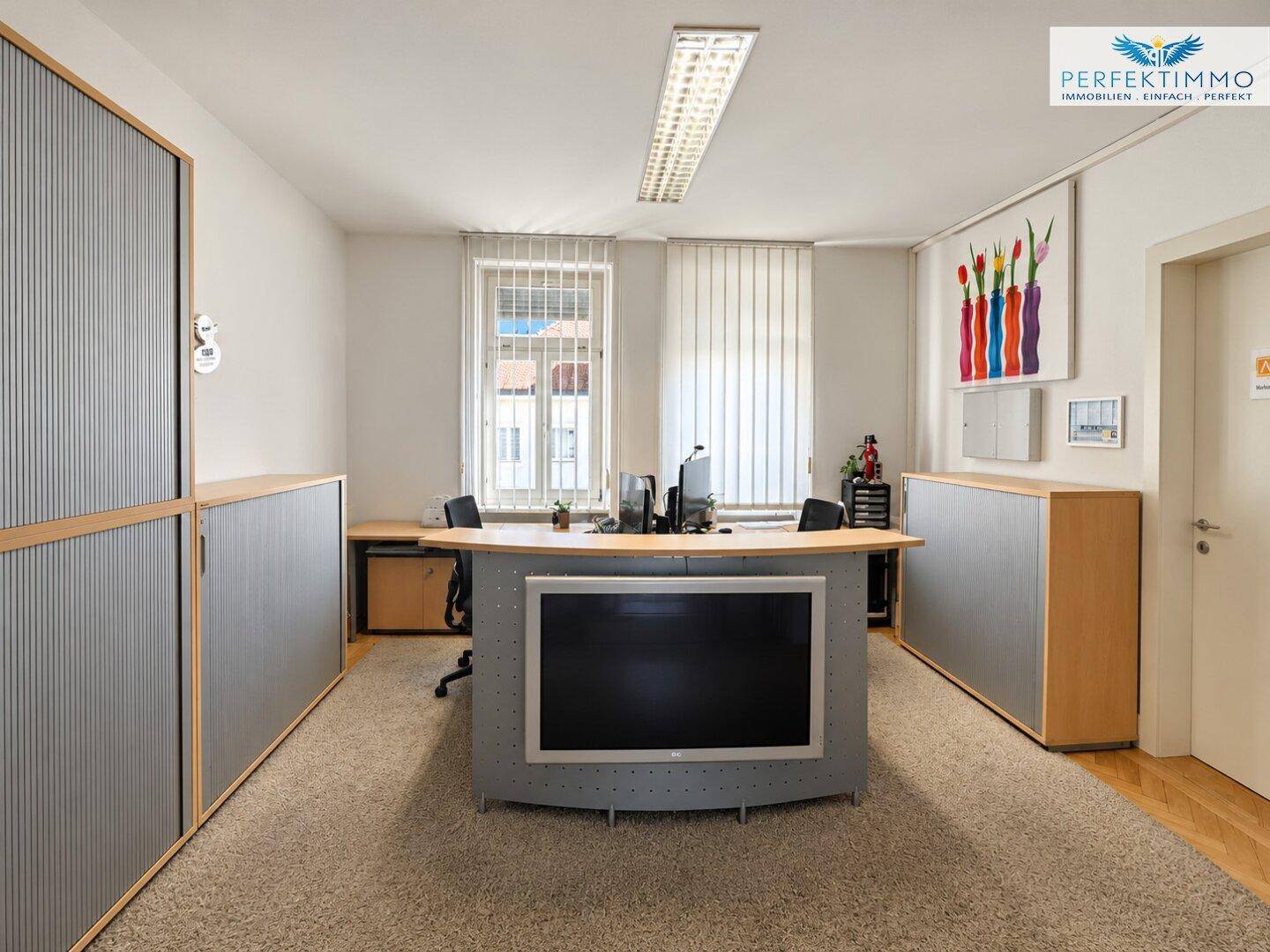 Geräumiges Büro mit Teppichboden, integrierten Schränken und einem großen Bildschirm.