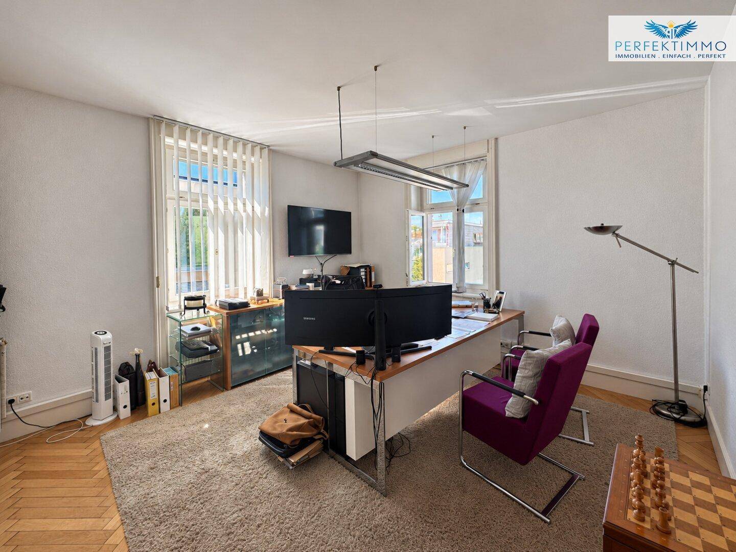 Geräumiges Büro mit Teppichboden, großem Schreibtisch und einem Fernseher.
