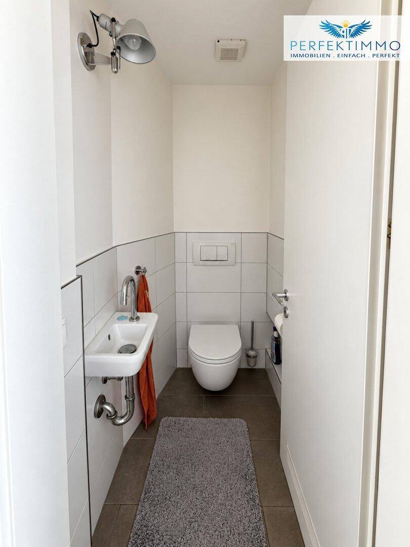 Modernes Gäste-WC mit wandmontierter Toilette und kleinem Waschbecken.