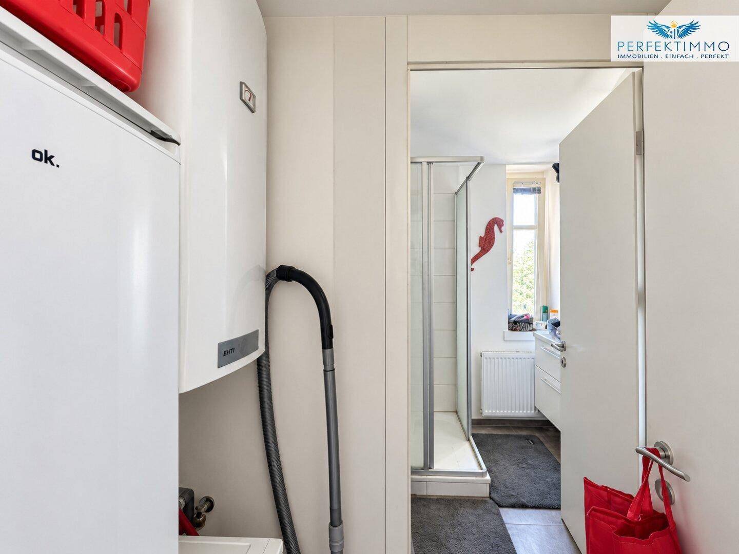 Hauswirtschaftsraum mit Boiler und Blick in ein Badezimmer mit Dusche.