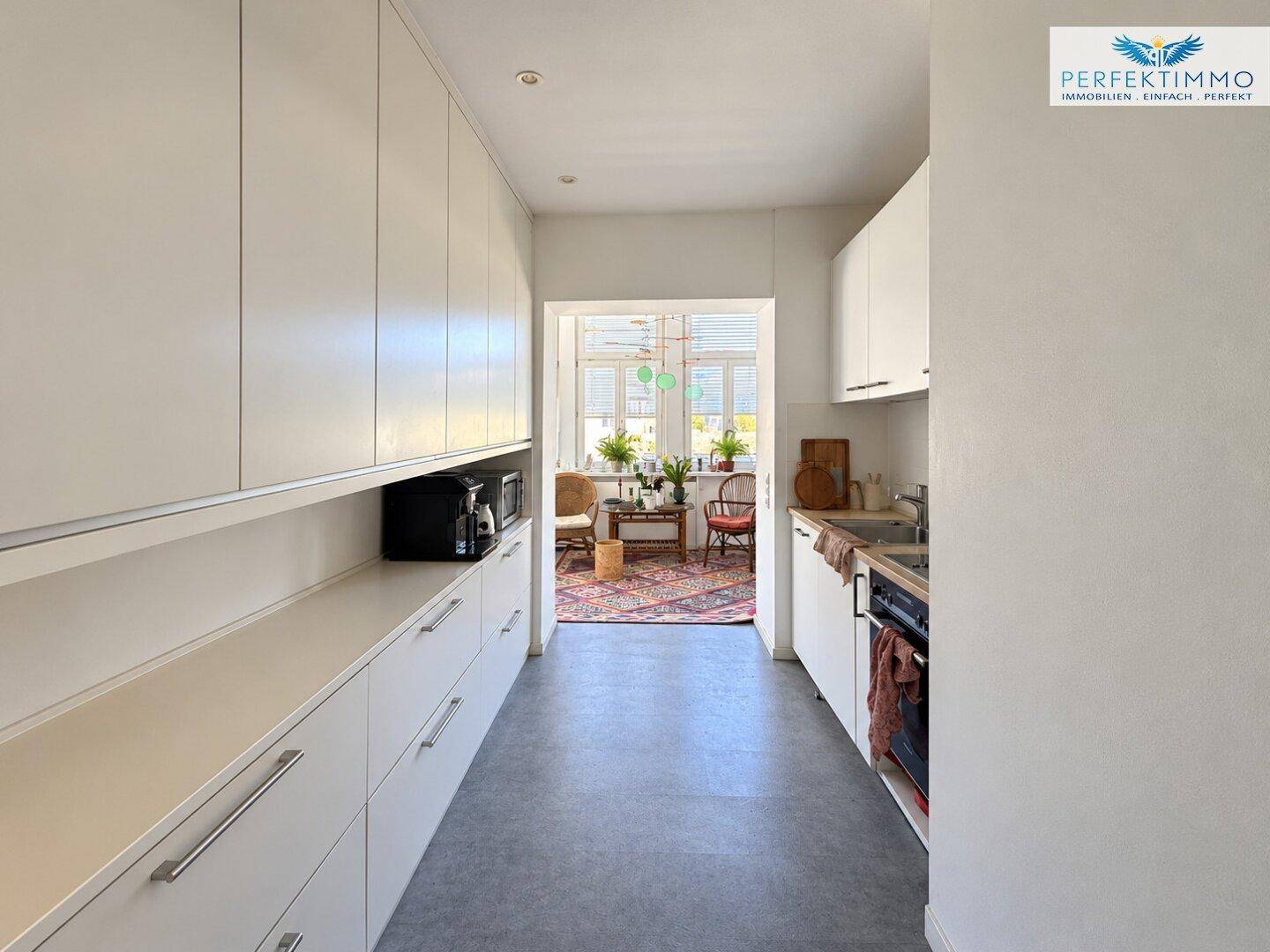 Moderne Küche mit weißen Schränken, integrierten Geräten und Blick in einen Wohnbereich.
