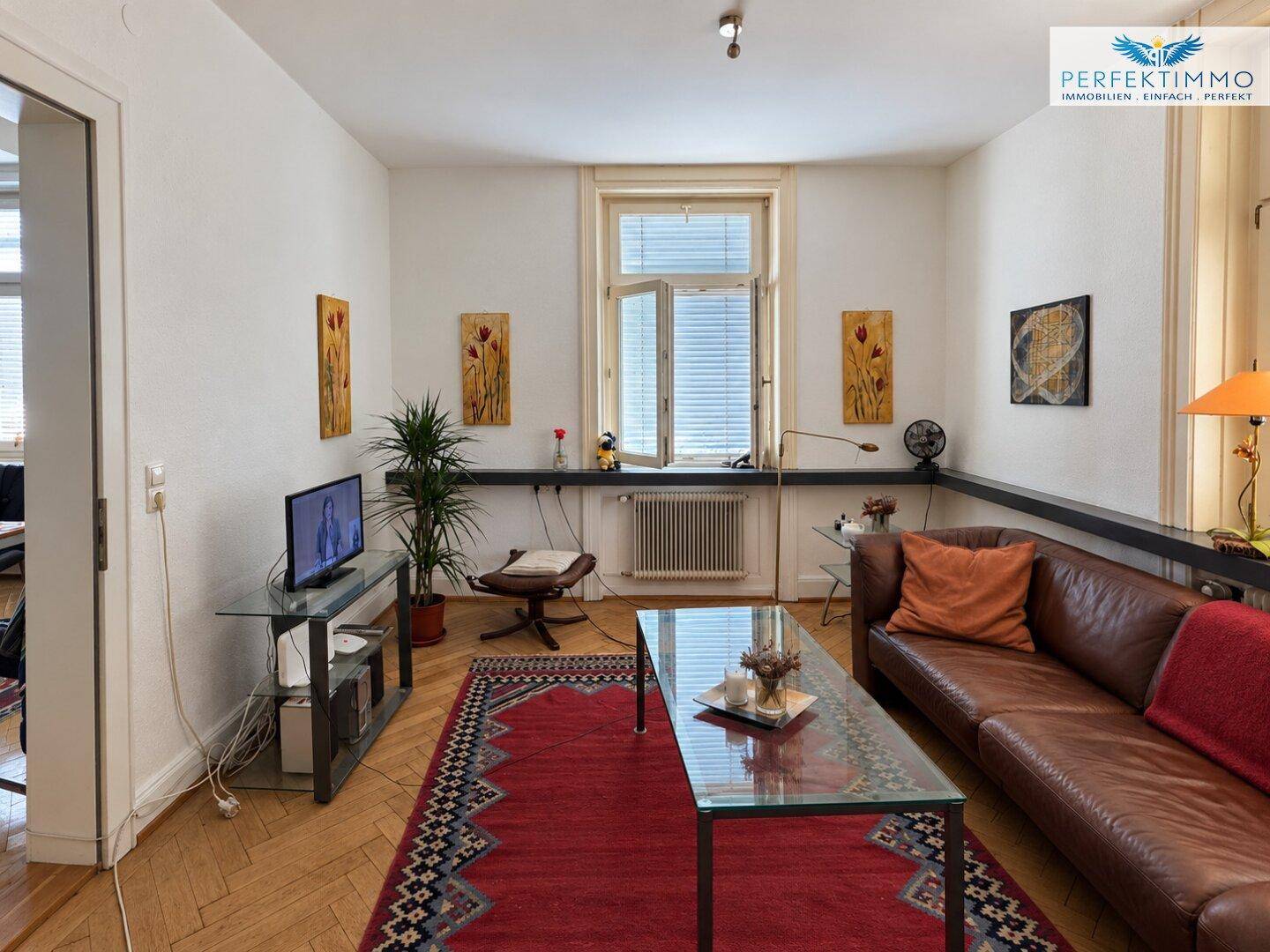 Gemütliches Wohnzimmer mit Ledersofa, Glascouchtisch und Fischgrätparkett.