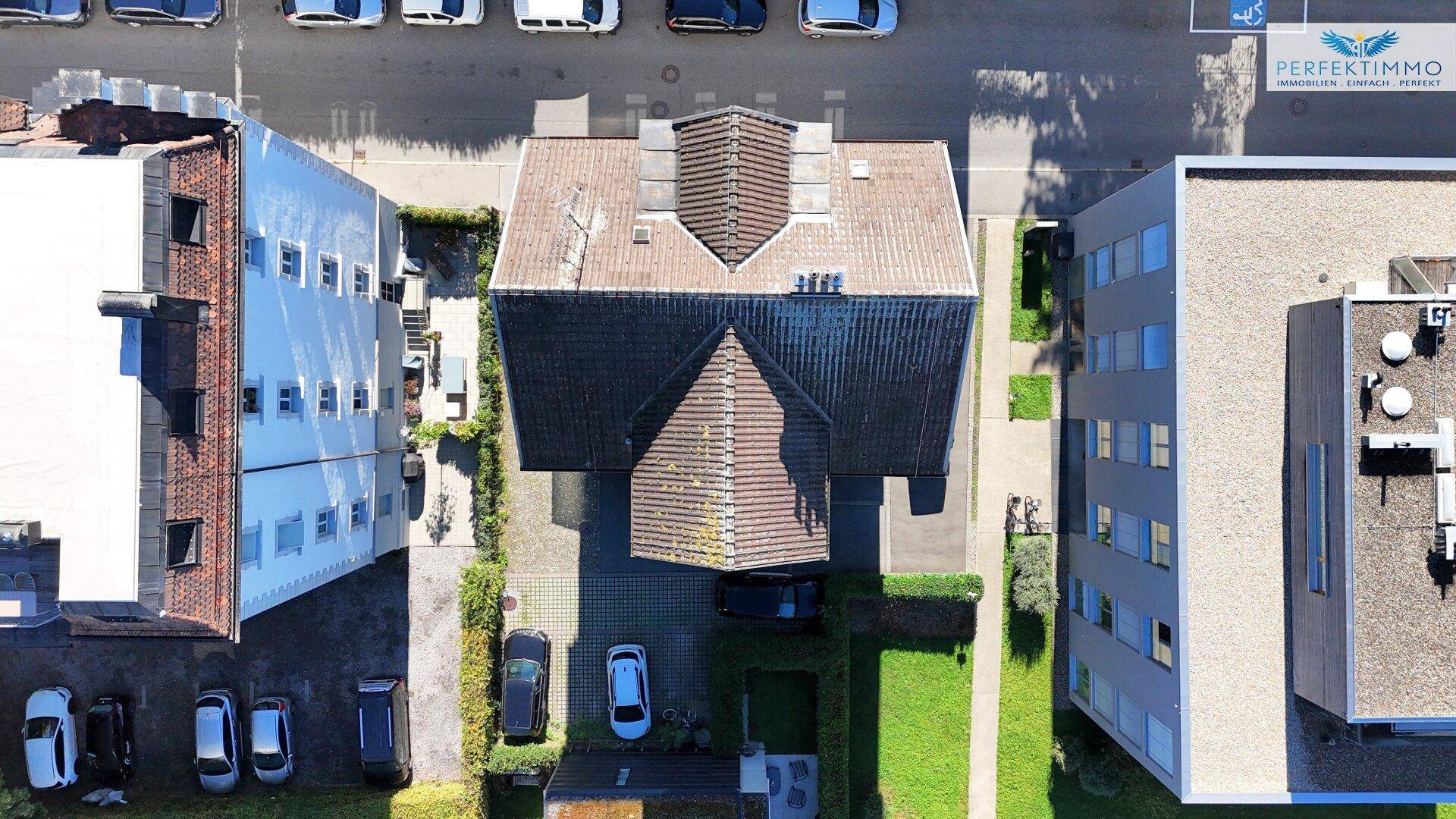 Senkrechte Luftaufnahme des Wohngebäudes mit Satteldach und angrenzenden Parkplätzen.