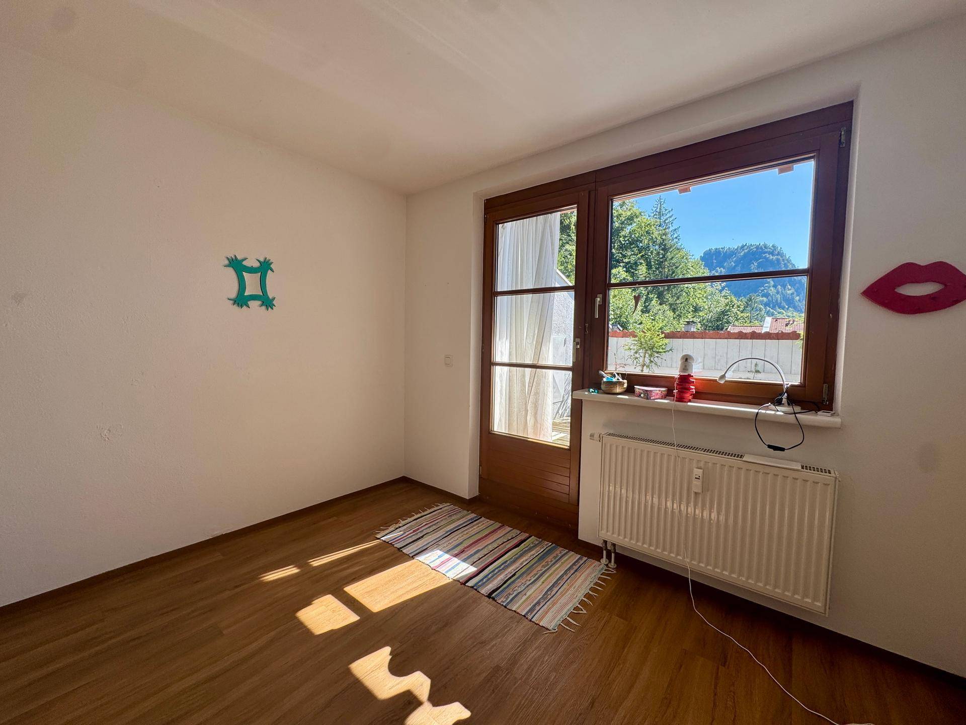 Helles Zimmer mit Laminatboden, großem Fenster und Zugang zu einem Außenbereich mit Bergblick.