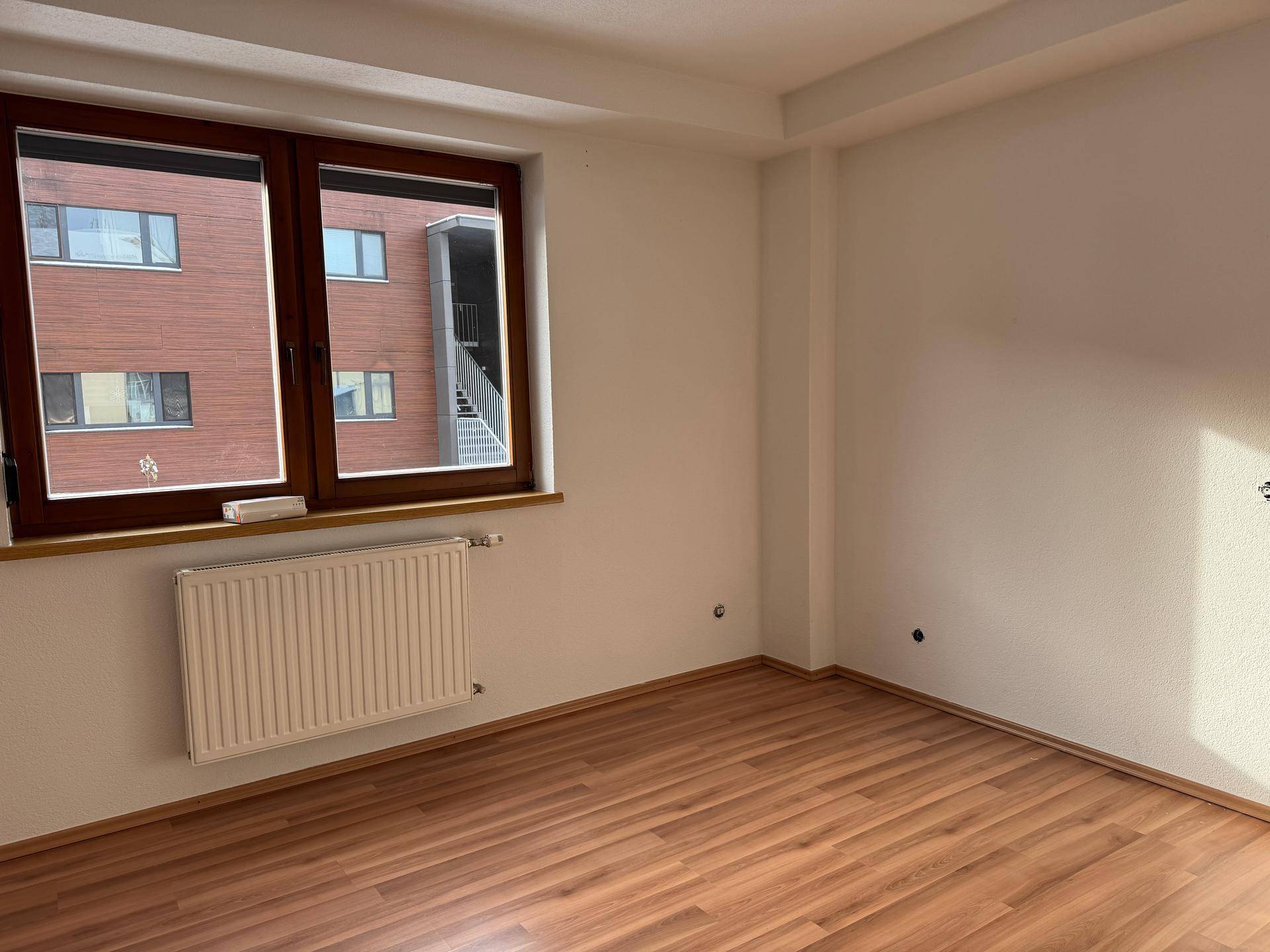 Leerer Raum mit Laminatboden, großem Fenster und Heizkörper.