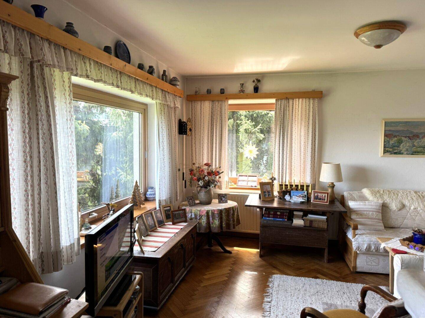 Helles Wohnzimmer mit traditionellen Holzmöbeln, Fischgrätparkett und Blick ins Grüne.