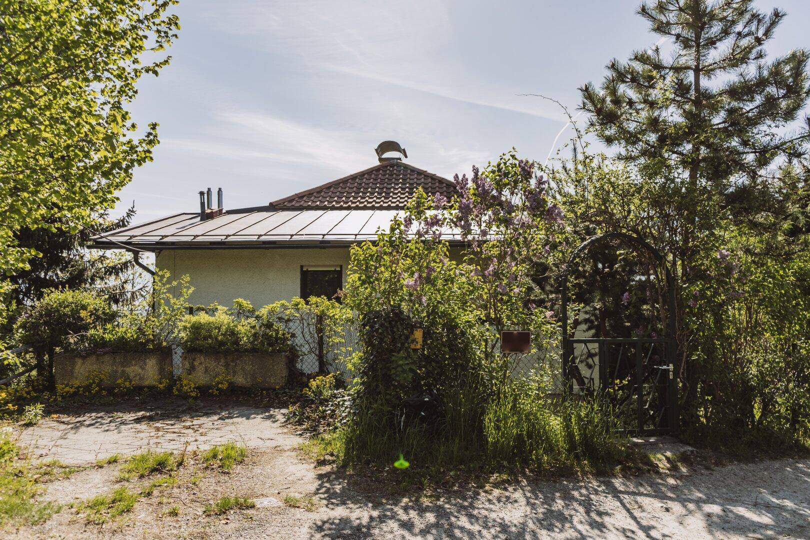 Hausfassade mit Ziegeldach und üppiger Vegetation im Vorgartenbereich.