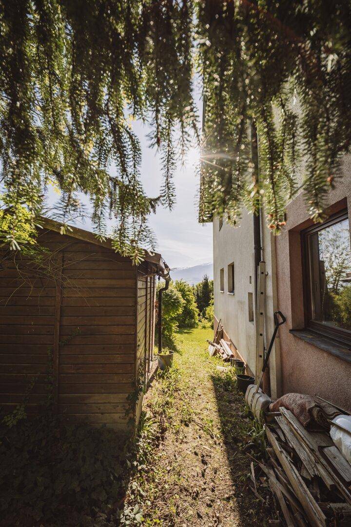 Seitenansicht des Hauses mit einem Holzschuppen und einem schmalen Gartenweg.