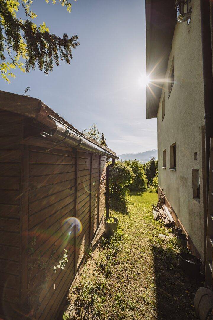 Sonniger Seitenbereich des Hauses mit Holzschuppen und Blick in die Ferne.