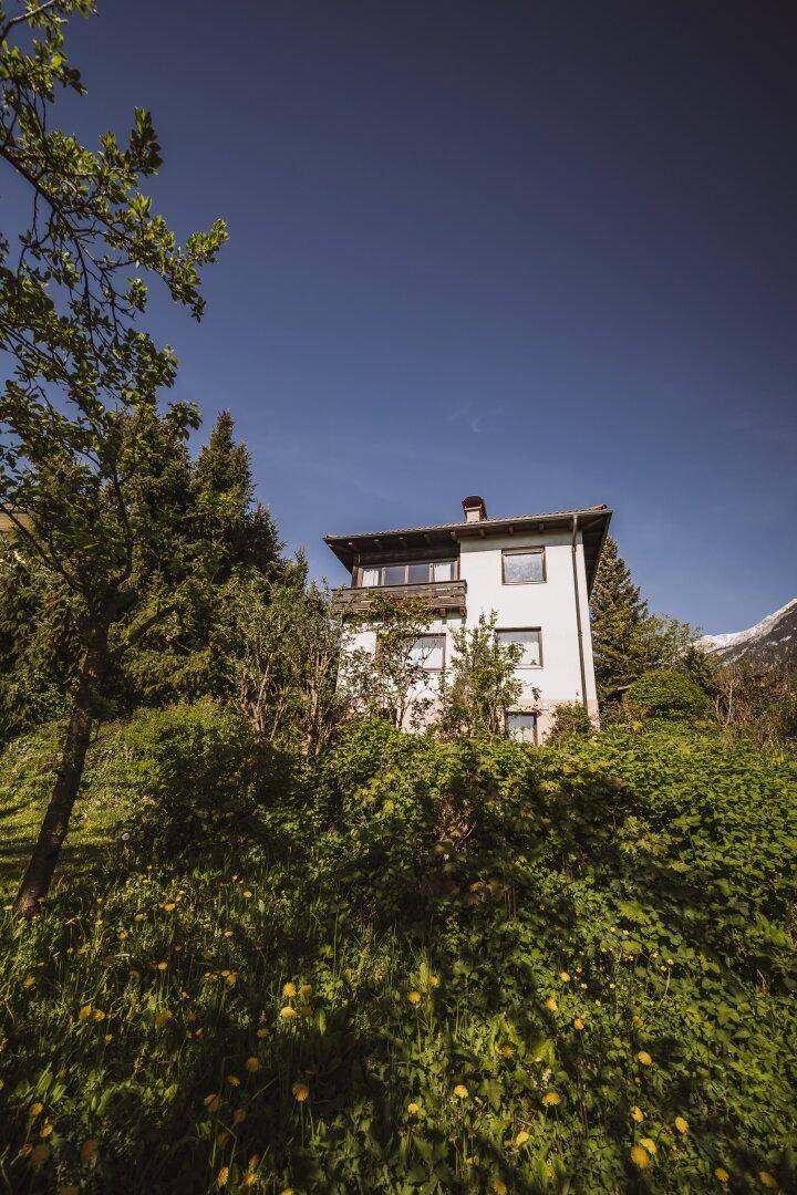 Hausfassade umgeben von üppigem Grün und einem klaren Blick auf die Berge.