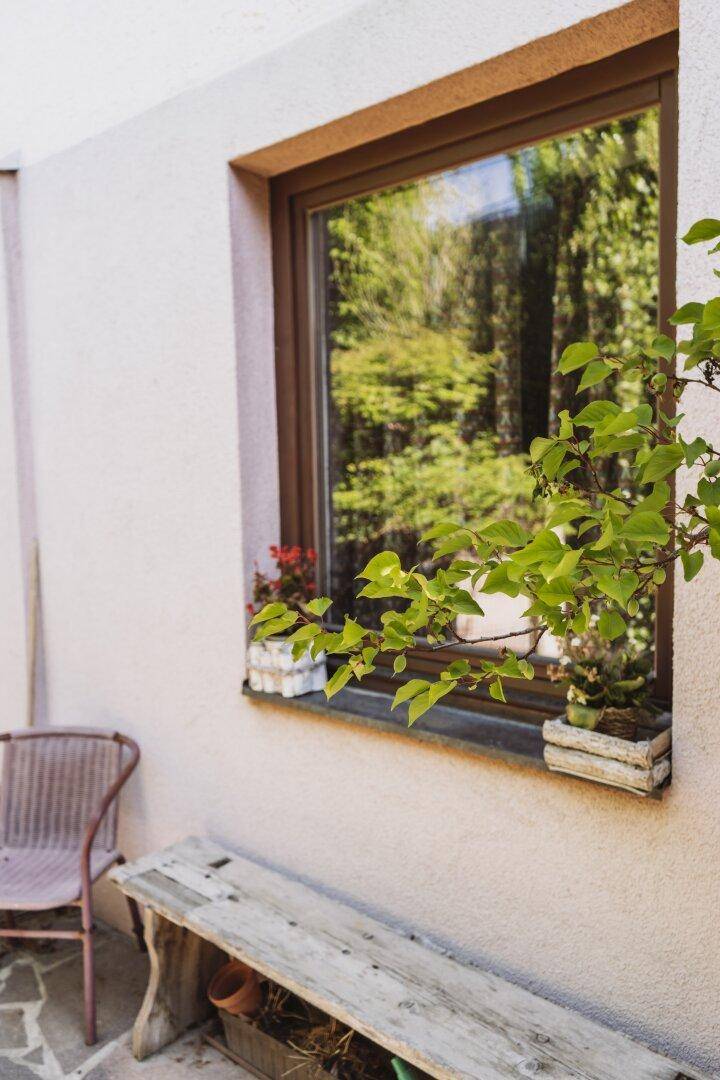 Fensterbereich mit kleiner Bank und Pflanzen auf der sonnigen Terrasse.