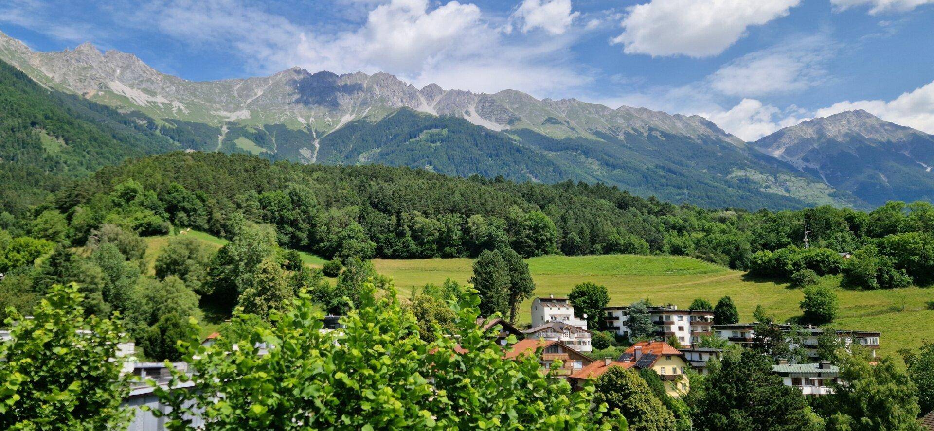 Panoramablick auf eine malerische Berglandschaft mit bewaldeten Hängen und Häusern.
