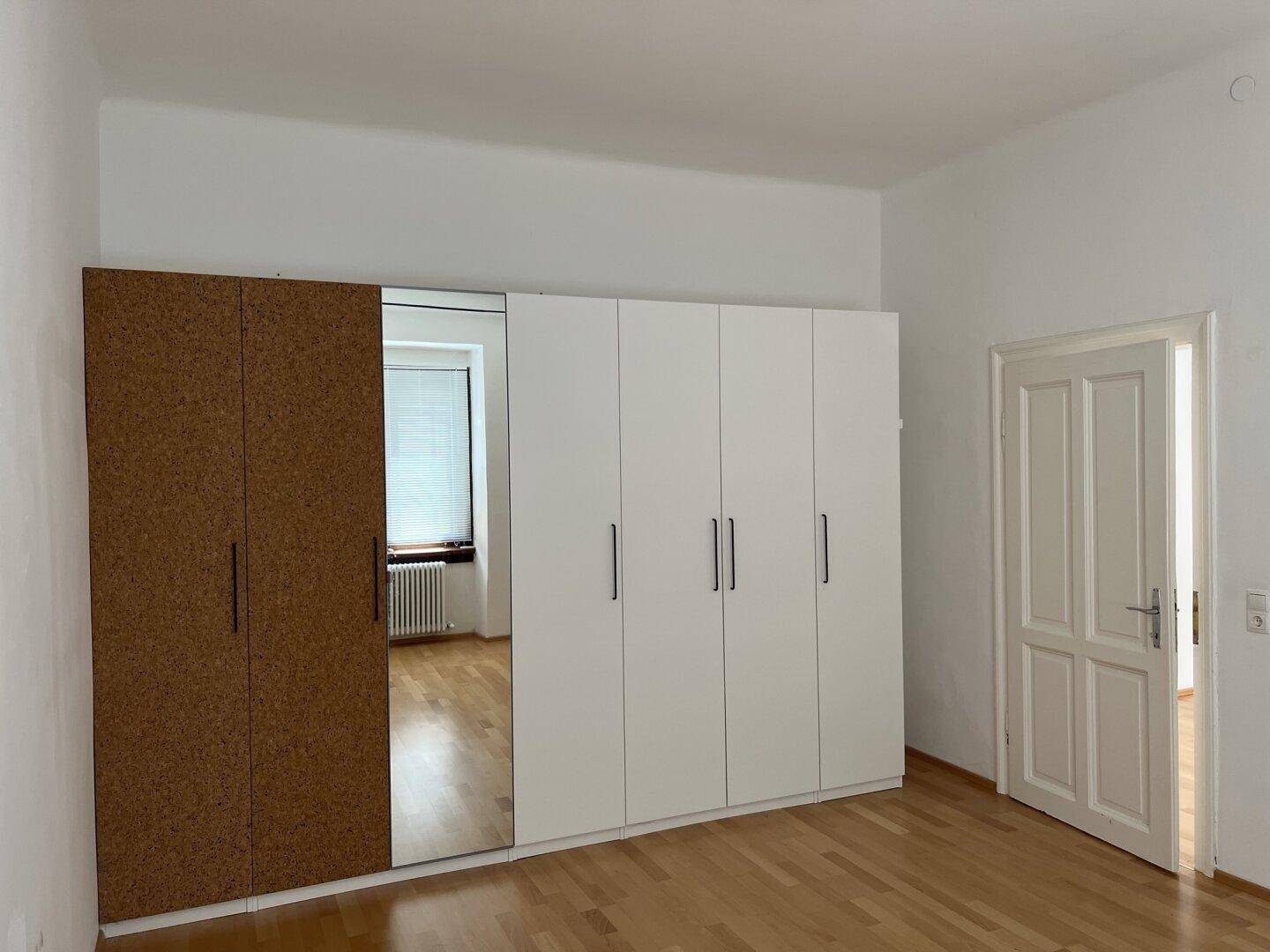 Schlafzimmer mit Parkettboden und großem Kleiderschrank mit Spiegel und Korkelementen.