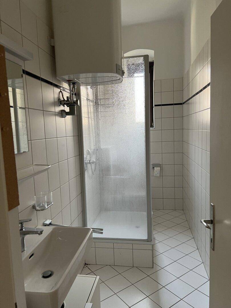 Gefliestes Badezimmer mit Duschkabine, Waschbecken und Warmwasserboiler.
