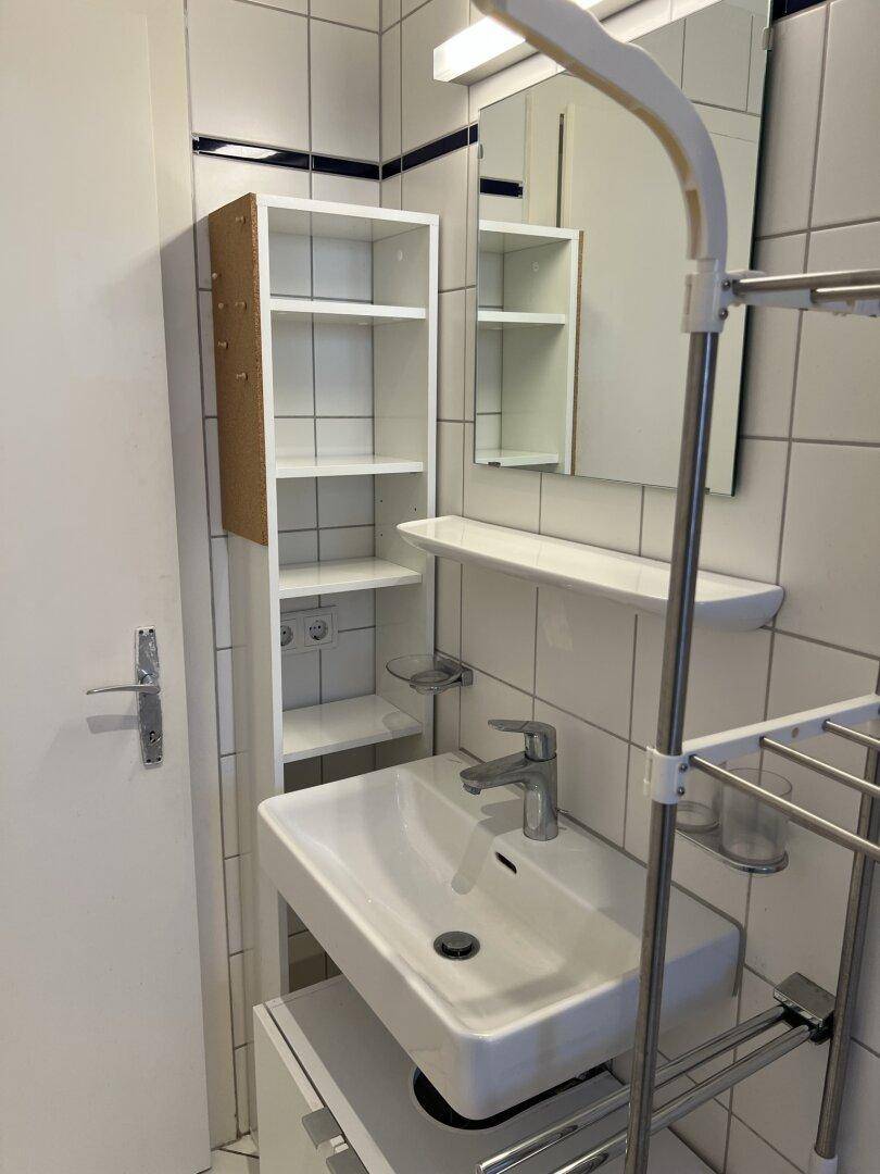 Badezimmer mit modernem Waschbecken, Spiegel und praktischen Ablageregalen.