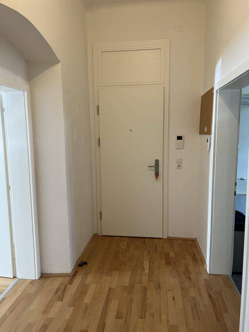 Heller Flur einer Wohnung mit Parkettboden und weißer Eingangstür.