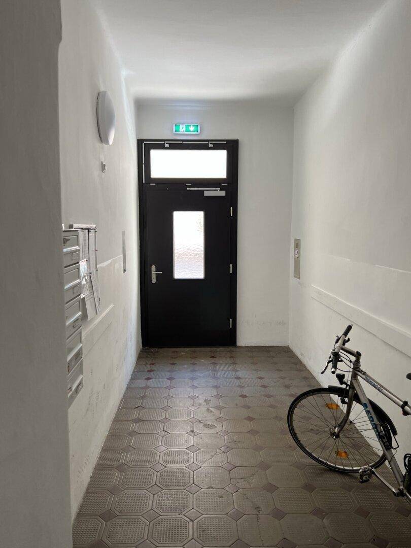 Heller Eingangsbereich eines Mehrfamilienhauses mit Fliesenboden und Fahrrad.