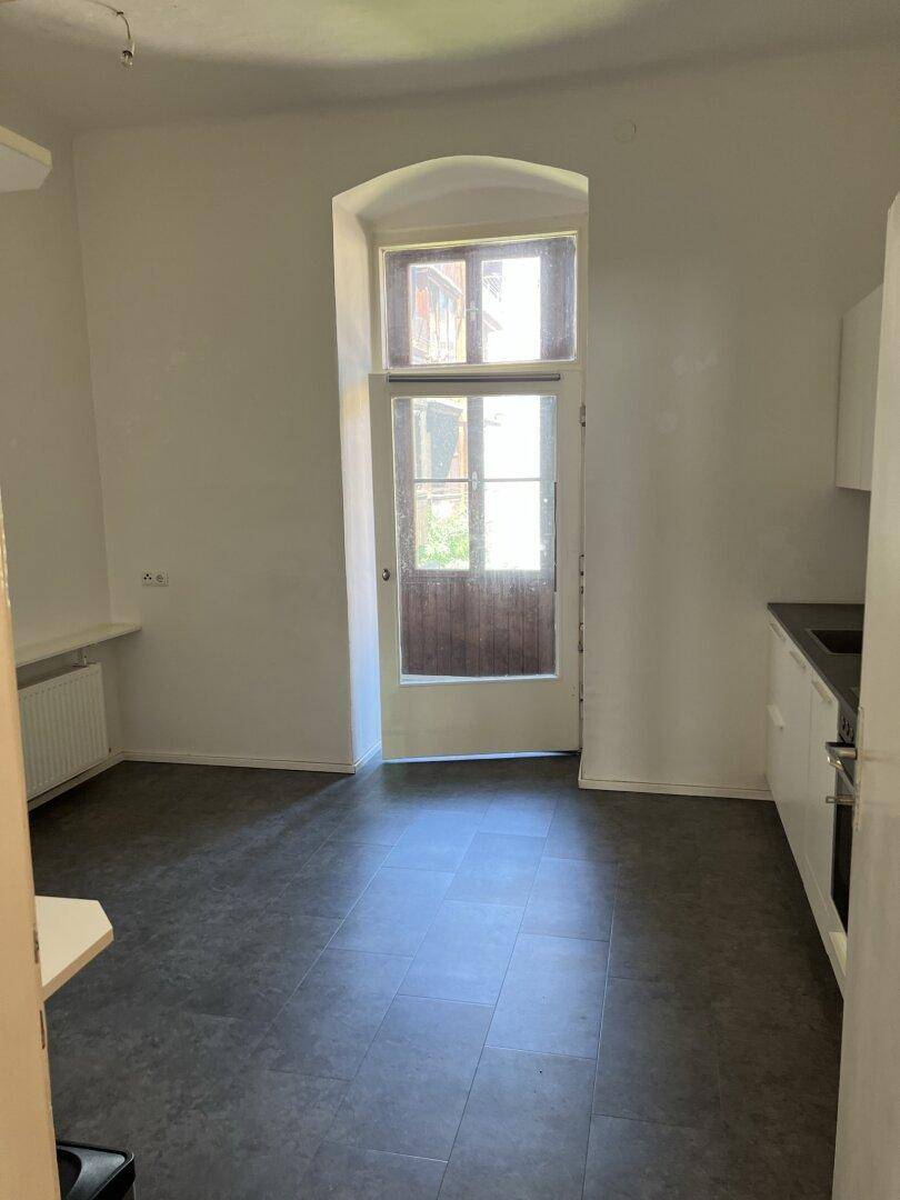 Geräumige Küche mit dunklem Boden, weißer Küchenzeile und hoher Fenstertür.