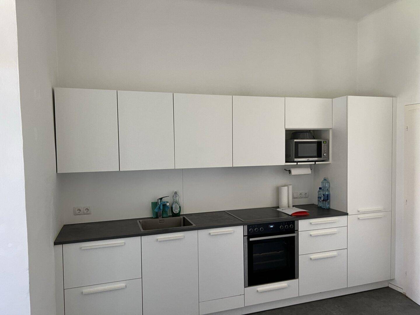 Helle Einbauküche mit weißen Schränken, dunkler Arbeitsplatte und integriertem Backofen.