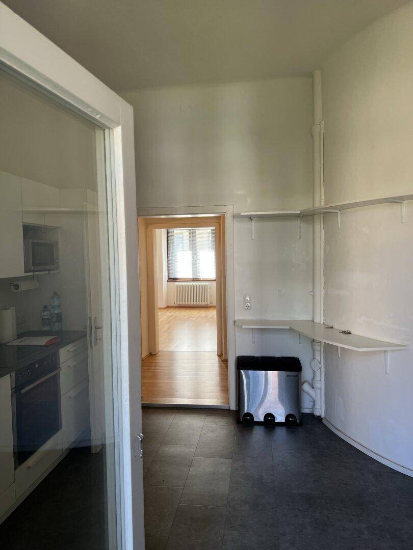 Küche mit dunklem Boden und Blick durch die Tür in ein Zimmer mit Parkettboden.