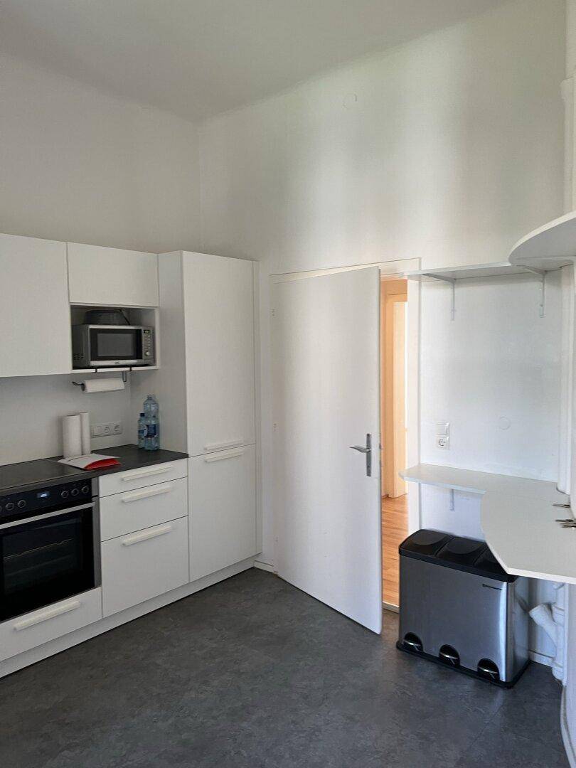 Moderne weiße Küche mit Einbaugeräten, dunkler Arbeitsplatte und Blick in den Flur.