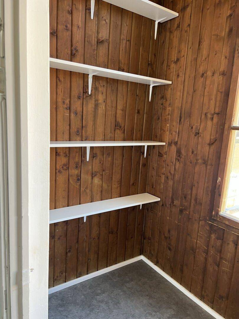 Kleiner Abstellraum mit Holzvertäfelung und praktischen weißen Regalen.