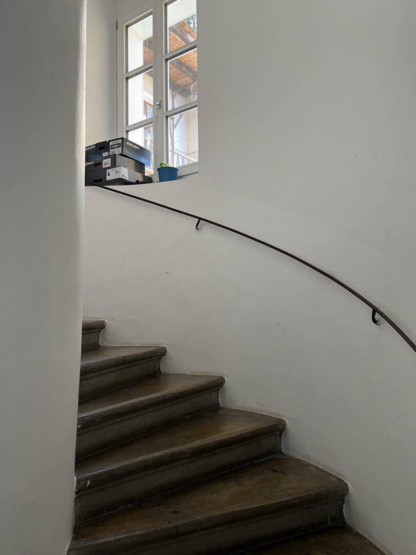 Treppenhaus mit Holzstufen, schlichtem Geländer und Fenster für natürliches Licht.