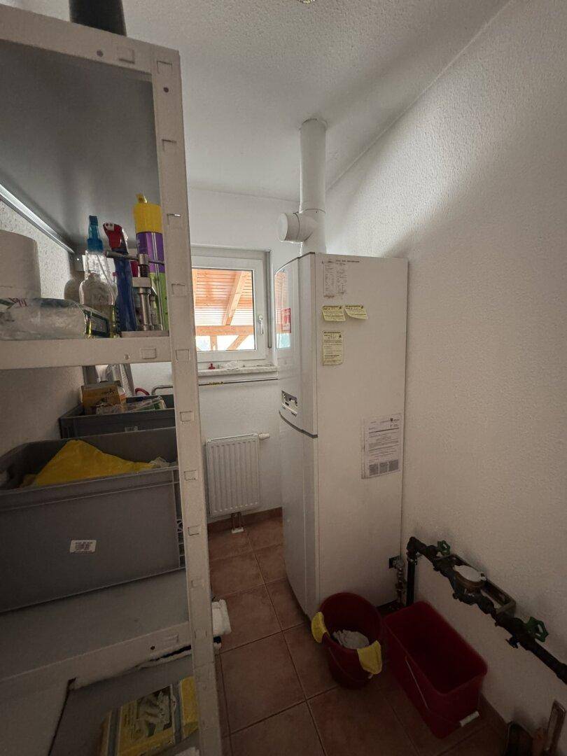 Praktischer Hauswirtschaftsraum mit Kühlschrank, Regalen und Fenster für natürliche Belüftung.