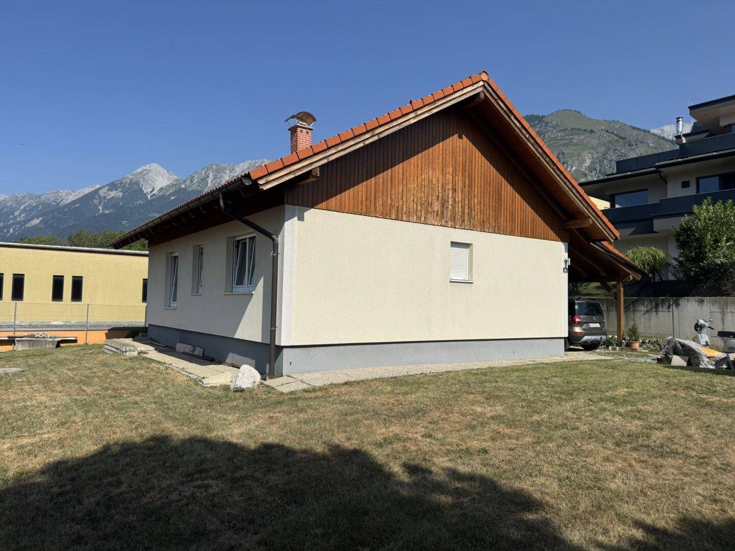 Seitenansicht des Hauses mit Rasenfläche, Carport und Bergbpanorama im Hintergrund.