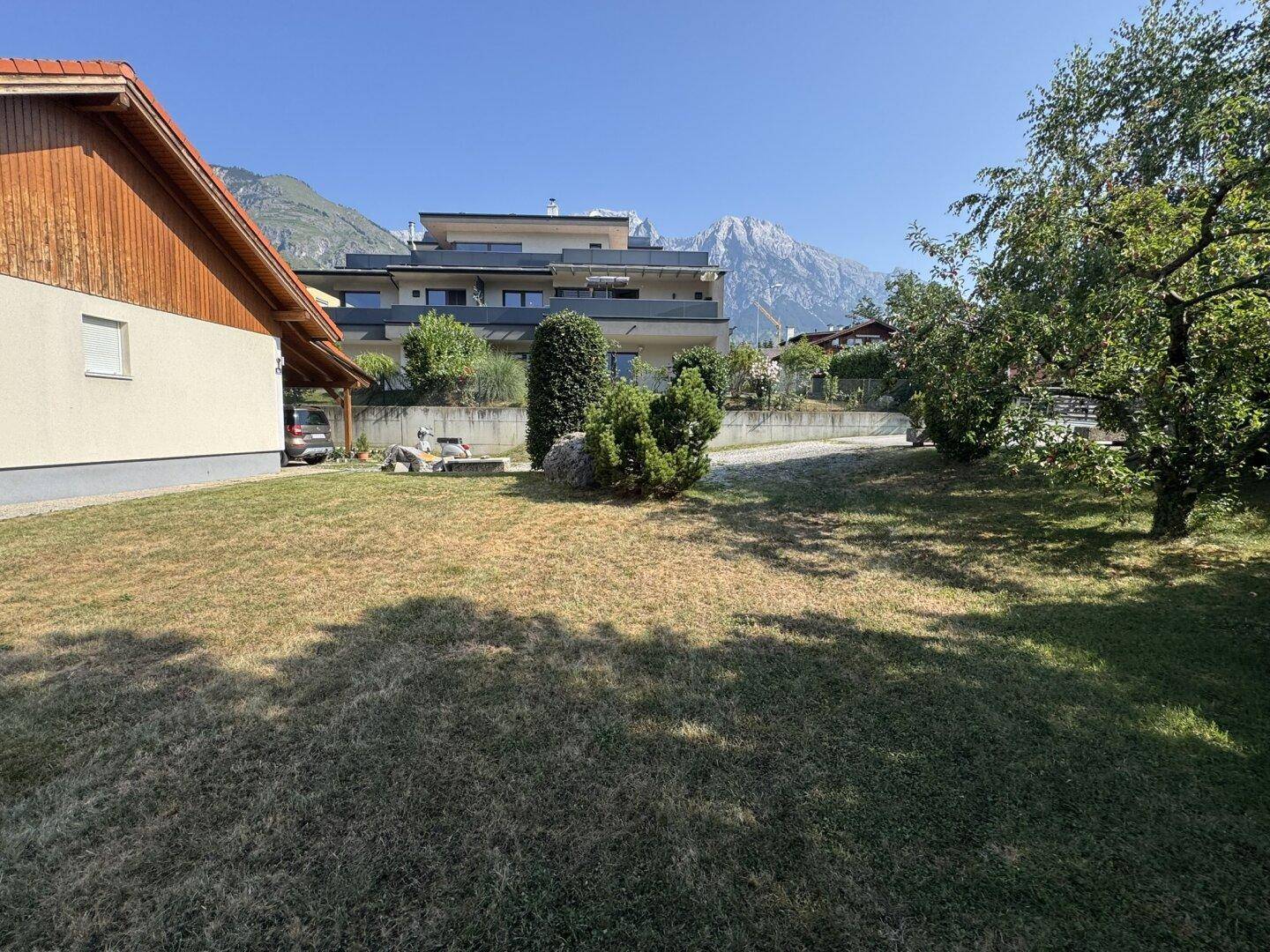 Gartenbereich mit Bäumen und Blick auf die Berge und Nachbargebäude.