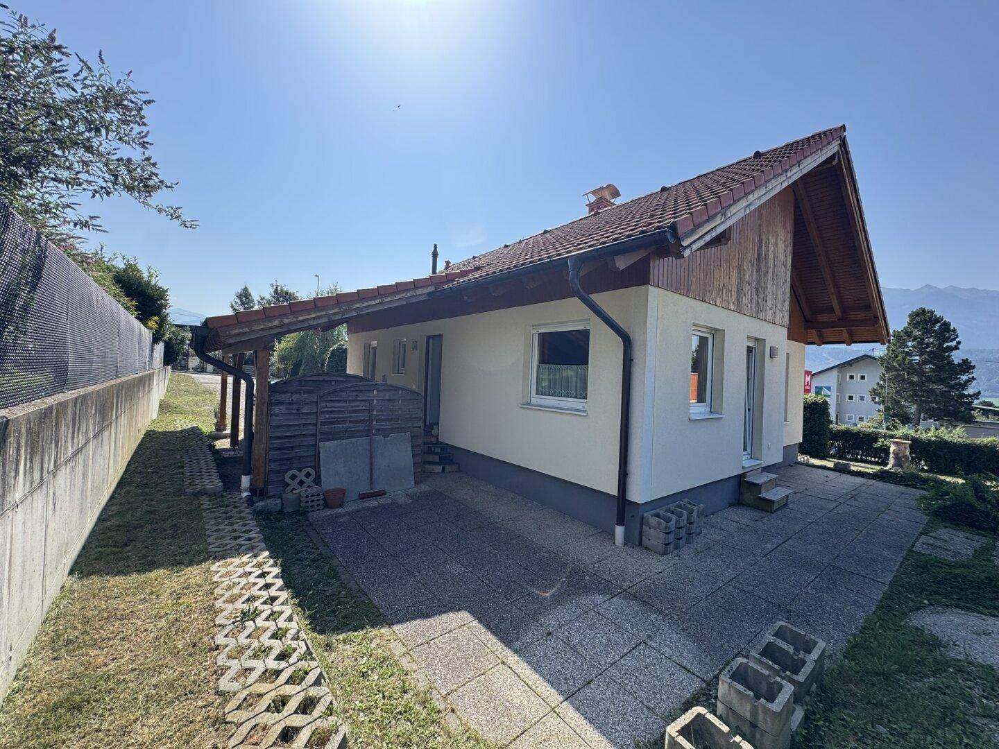 Seitliche Terrasse mit Pflastersteinen und überdachtem Bereich am Haus.
