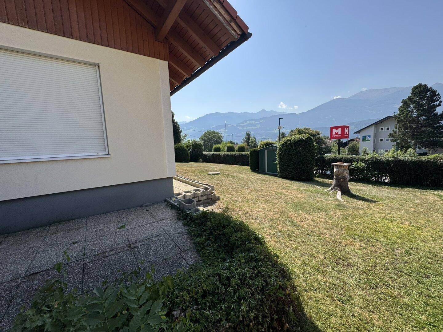 Großer Gartenbereich mit Rasen, Hecken und Blick auf die Umgebung an einem sonnigen Tag.