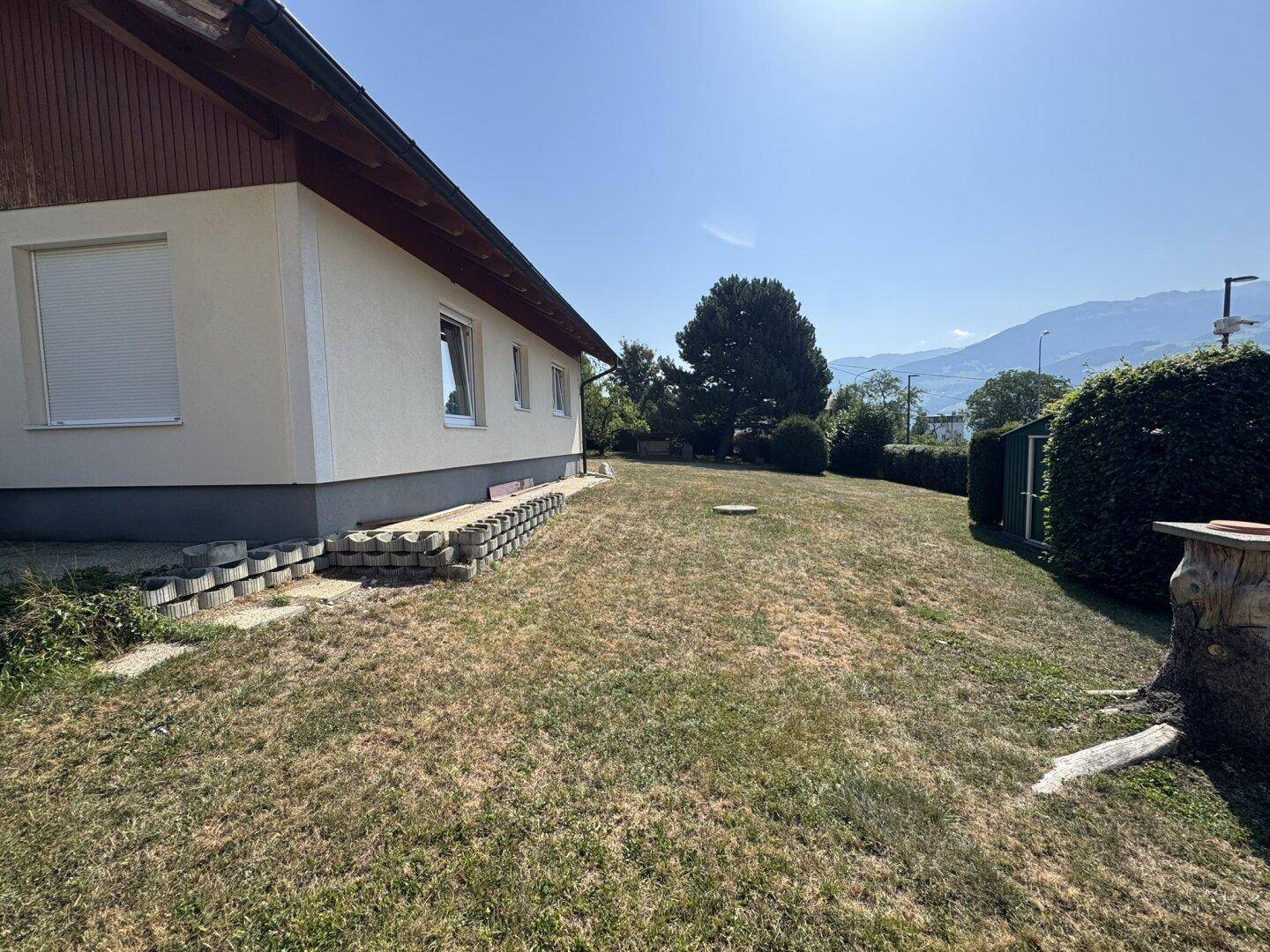 Seitenansicht des Hauses mit weitläufigem Garten und Hecken unter blauem Himmel.