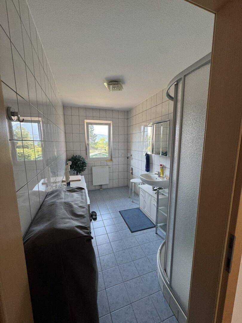Badezimmer mit Duschkabine, Fliesenboden und Fenster, gut beleuchtet.