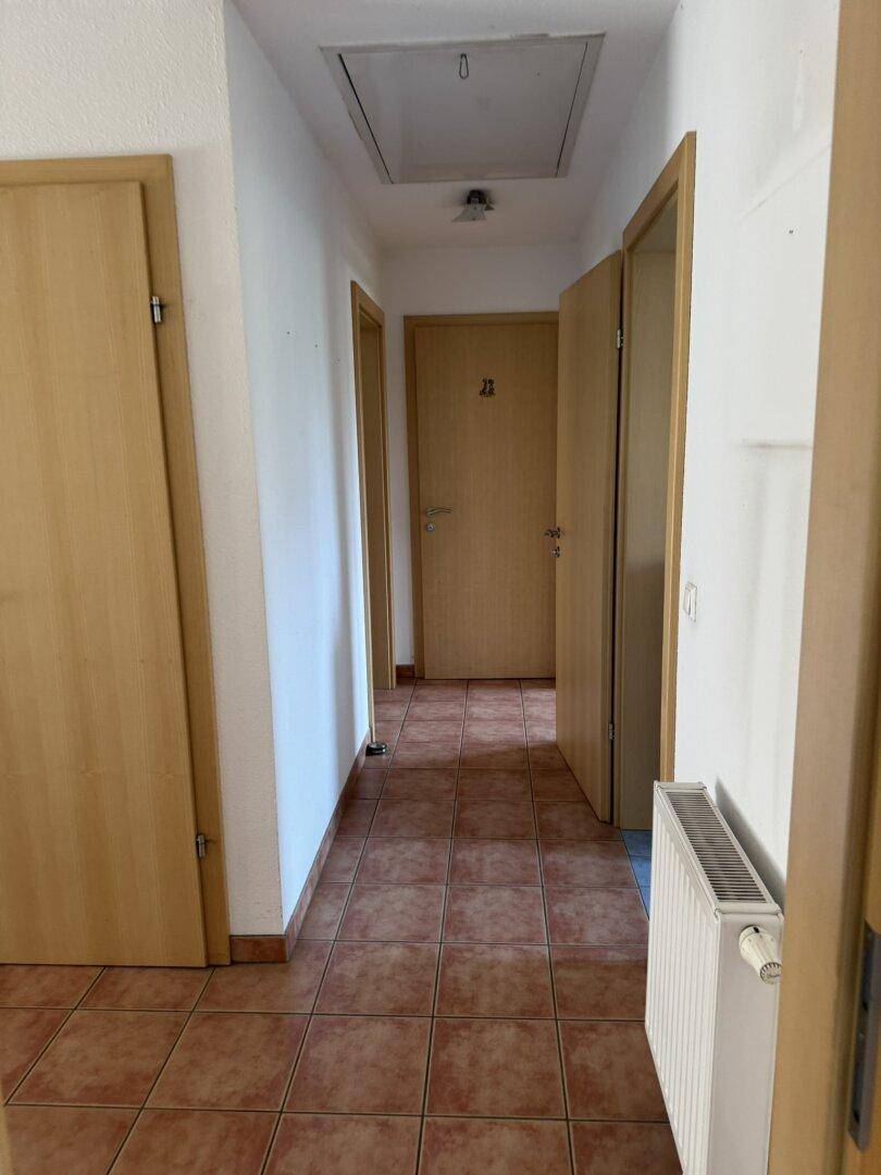 Flur mit Fliesenboden, Heizkörper und Zugangsluke zur Decke.