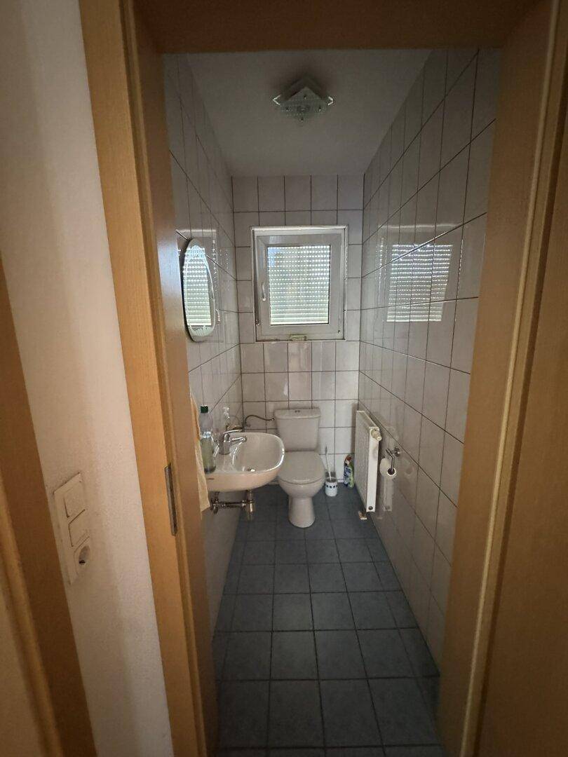 Schmales Gäste-WC mit Fliesenboden, Fenster und Wand-WC in Standardausführung.