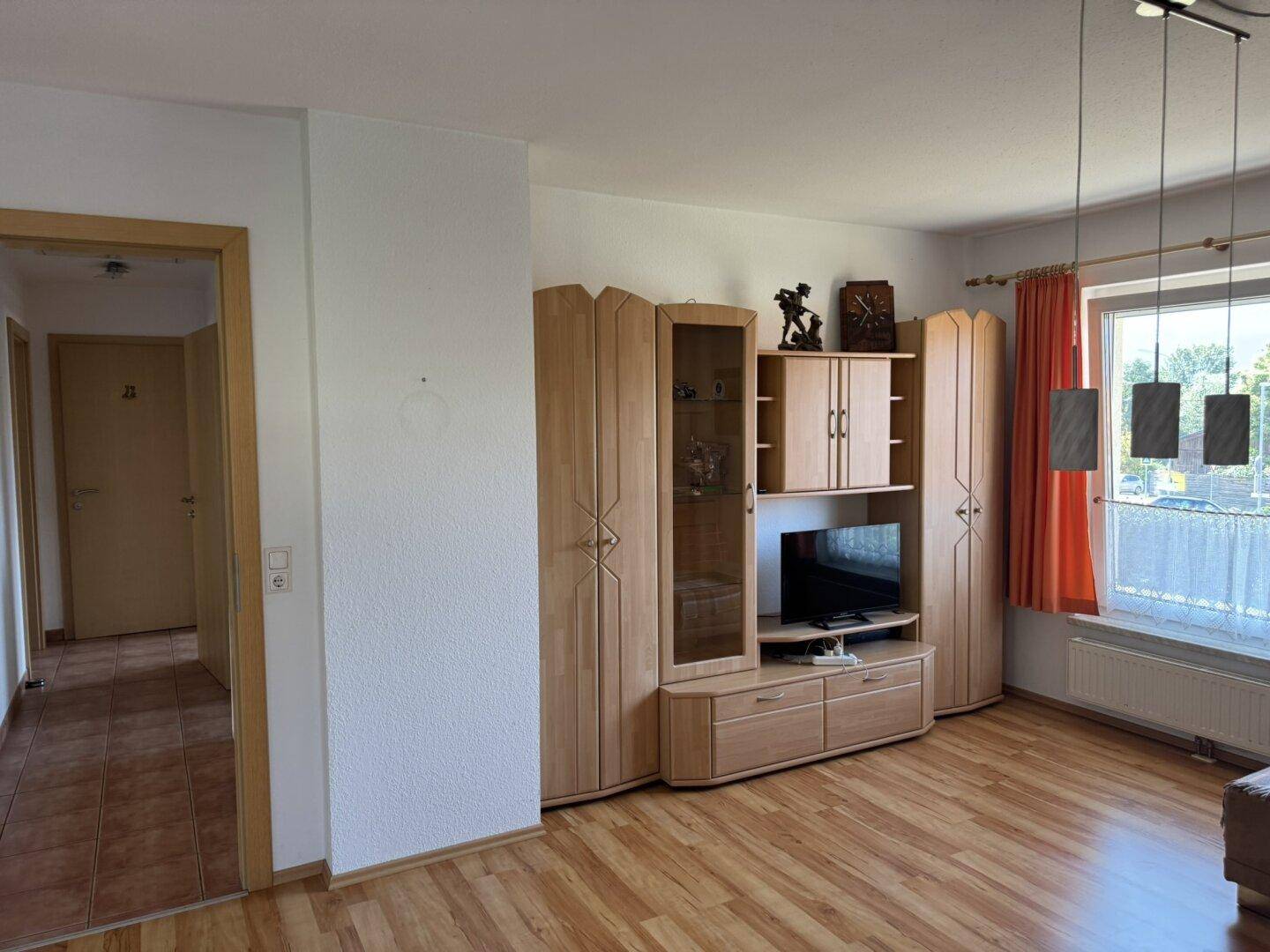 Gemütliches Wohnzimmer mit Laminatboden, großem Schrank und Fenster mit Vorhängen.