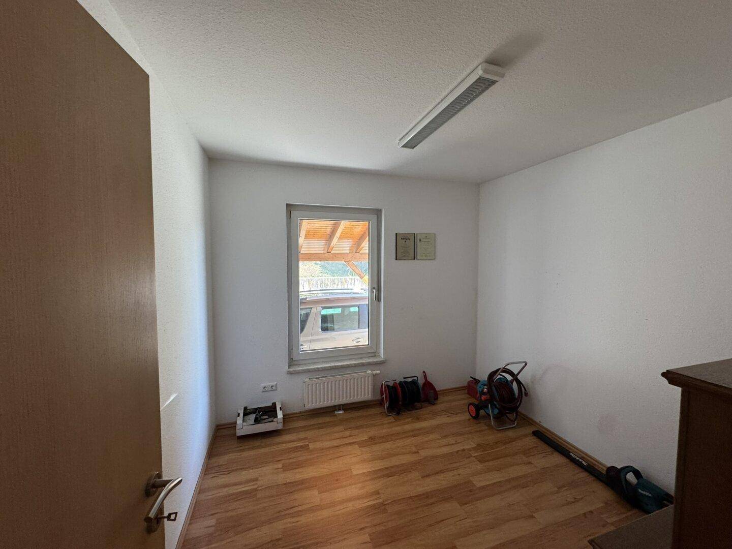 Leeres Zimmer mit Laminatboden, Fenster und Heizkörper, bereit zur Einrichtung.