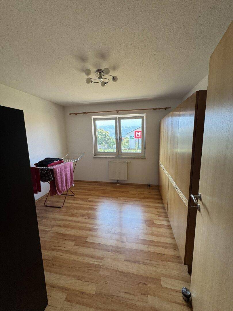 Schlafzimmer mit Laminatboden, großem Fenster und Kleiderschrank.