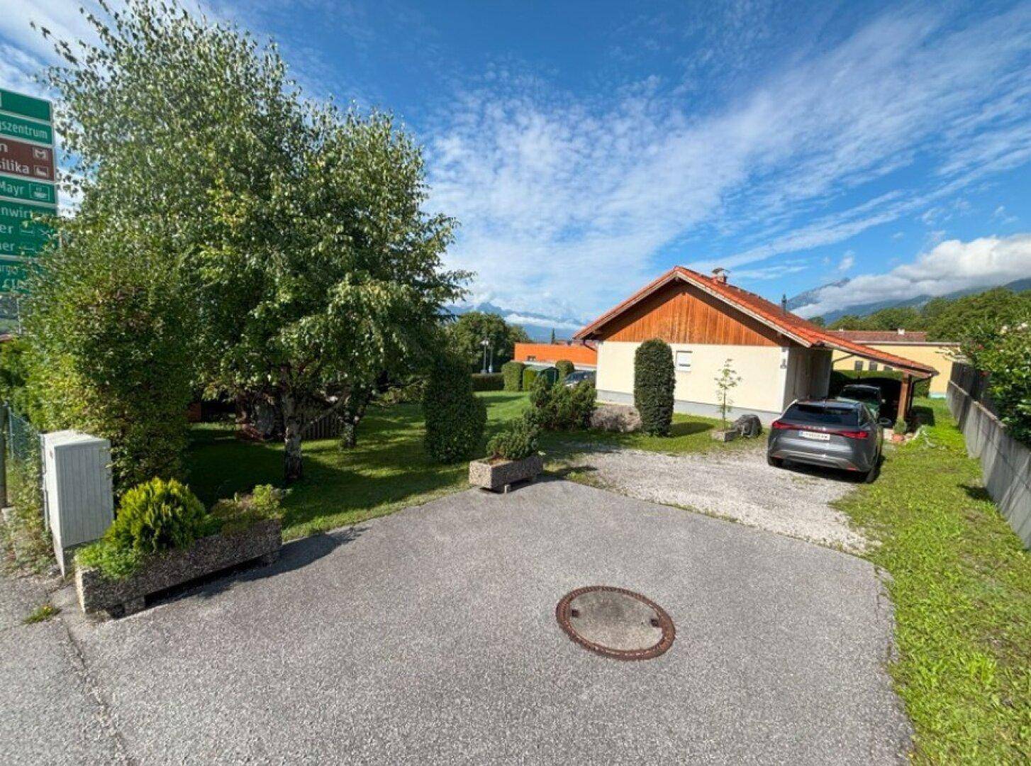 Vorderansicht des Hauses mit Einfahrt, Carport und Bergblick unter blauem Himmel.