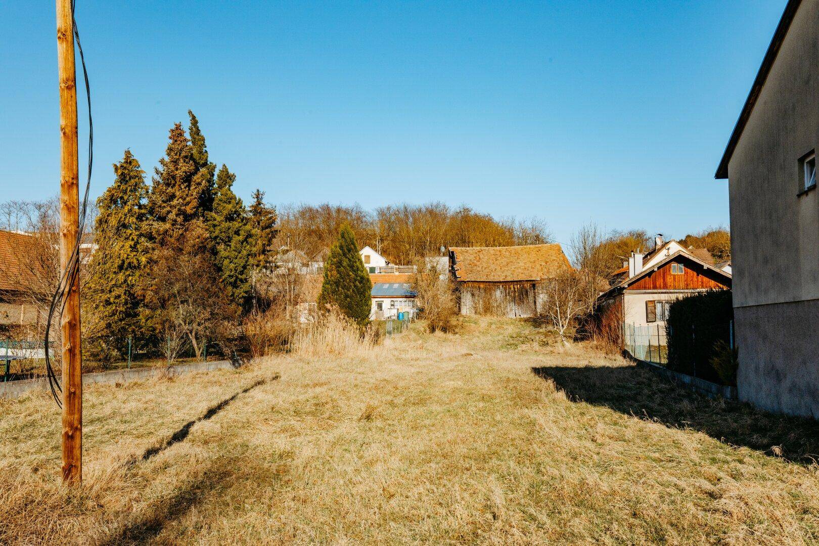 Weitläufiges, unbebautes Grundstück mit trockenem Gras und umgebenden Häusern unter klarem, blauem Himmel.