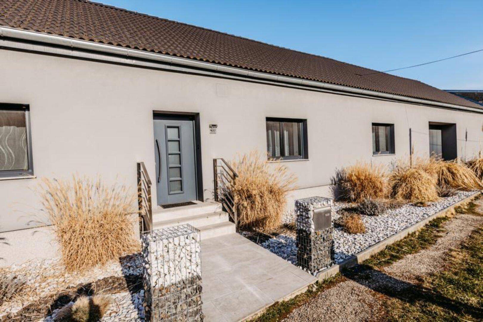 Eingangsbereich des Hauses mit moderner Tür, Gabionen-Elementen und einem gepflegten Zugangsweg.