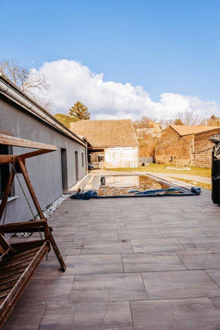Große geflieste Terrasse mit Schaukelbank und Blick auf den abgedeckten Poolbereich im Garten.