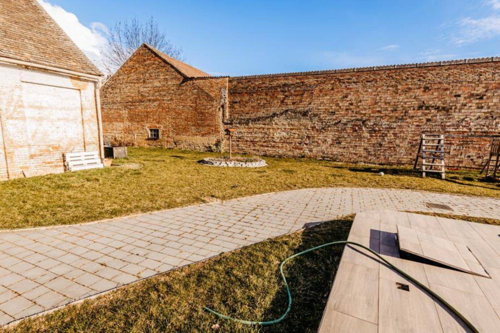 Gepflasterter Weg durch den Garten, umgeben von Rasenflächen und alten Ziegelmauern.