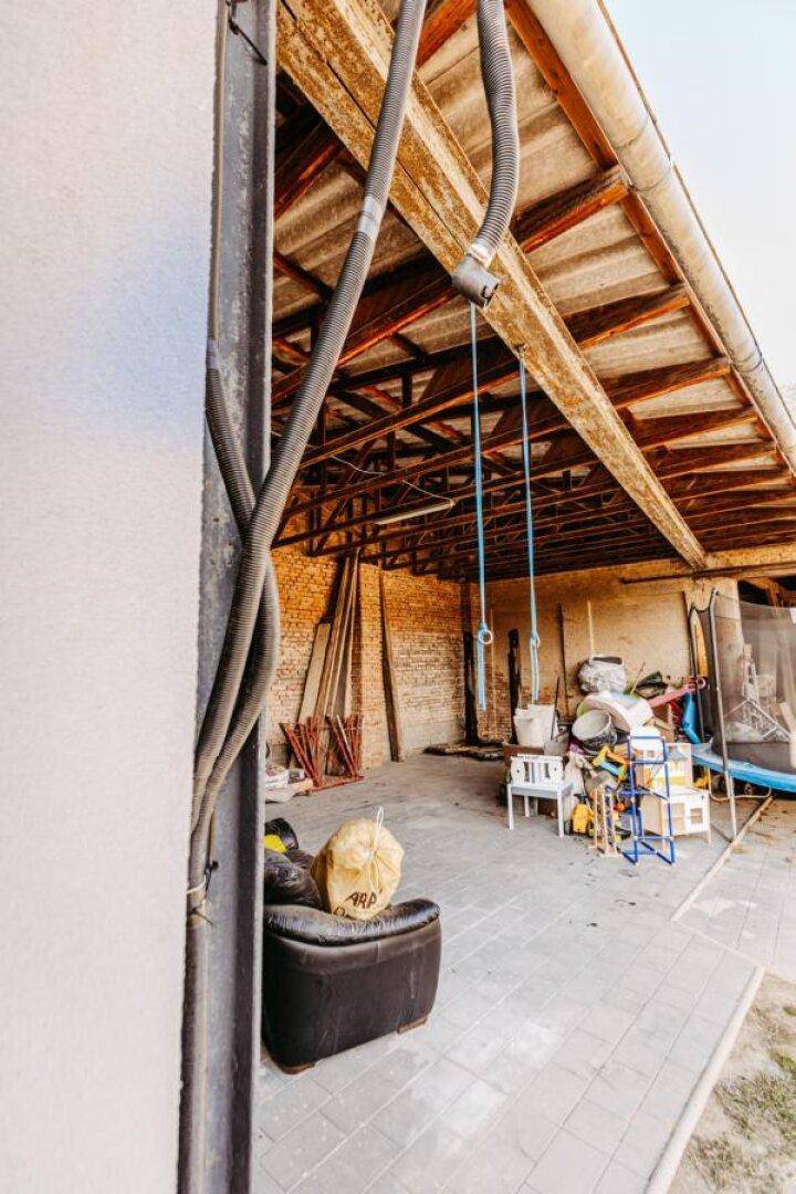 Offener Unterstand mit Holzbalkenkonstruktion, Ziegelwänden und verschiedenen Lagergegenständen.