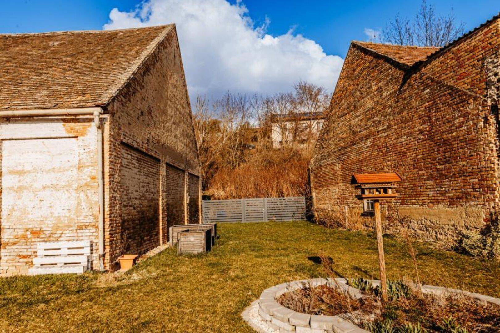 Gartenbereich zwischen zwei historischen Ziegelgebäuden mit Rasenfläche und einem Vogelhaus.
