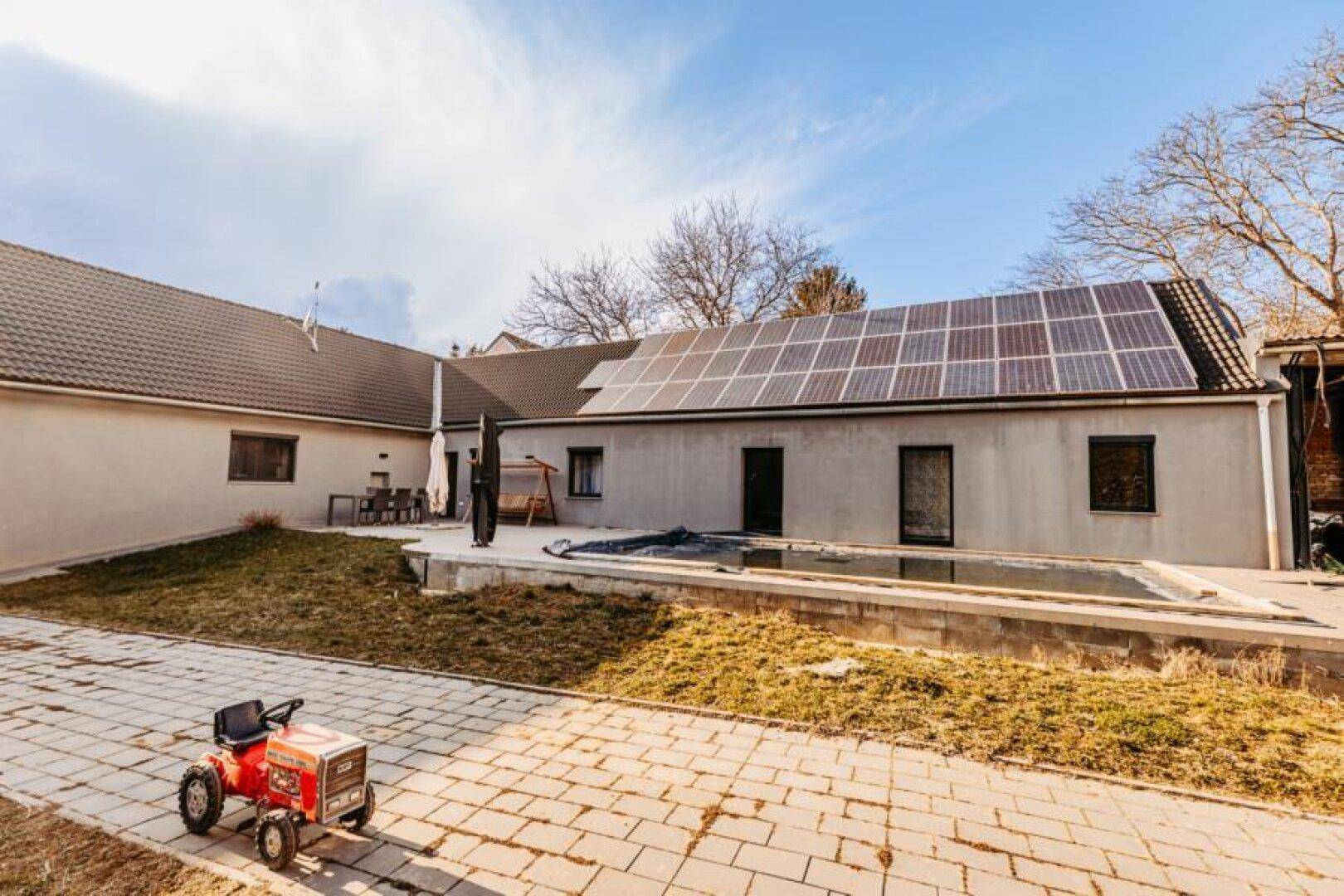 Rückseite des Hauses mit Photovoltaikanlage, Terrasse und dem abgedeckten Poolbereich.