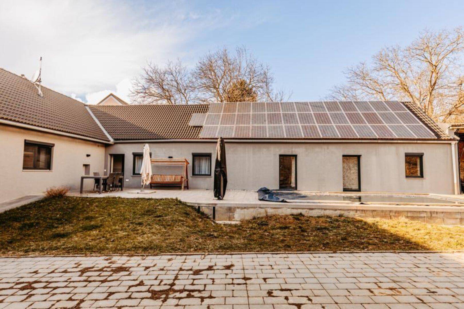 Weitläufige Ansicht der Hausrückseite mit Solaranlage, Terrasse und dem Poolbereich.